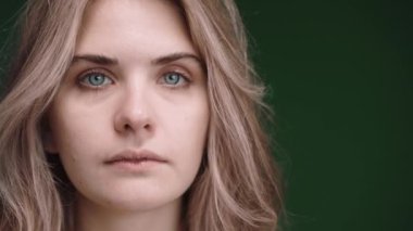 Close shot of woman turning from sad to happy smiling, standing in green studio