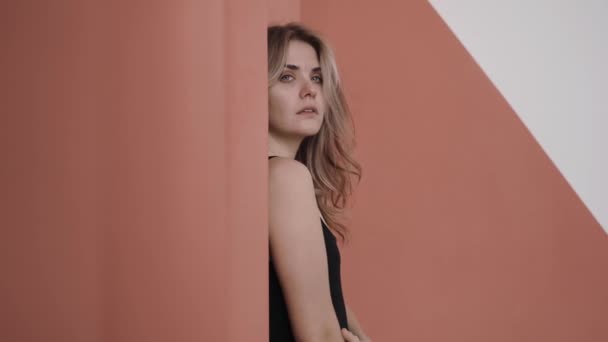 Close shot of woman turning from sad to happy smiling, standing in pink studio — Stockvideo