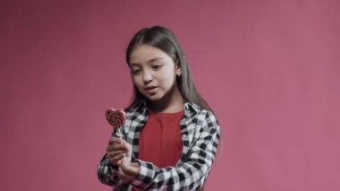 Little girl is happy with heart caramel on a stick, surprised emotion