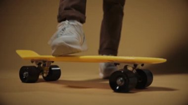 Boy puts one foot on a yellow penny board, close shot