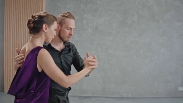 Mann und Frau tanzen aktiv einen Tango in einem grauen Raum mit großen Fenstern — Stockvideo