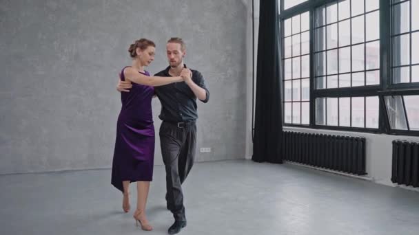 Hombre y mujer bailan sensualmente un tango en un salón luminoso con grandes ventanales — Vídeos de Stock