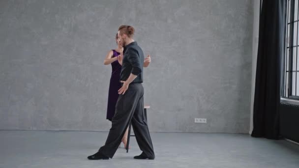 Man showing woman tango elements in grey studio against large windows — Stock Video