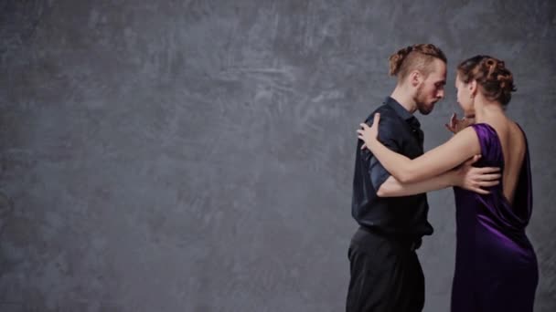 Mężczyzna i kobieta zmysłowo tańczą tango w szarym studio — Wideo stockowe