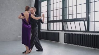 Bir çiftin büyük pencerelerin arka planında tango yaparak şehvetle dans etmesi.