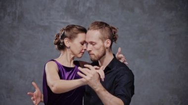 Tango dansçısı bir kadına sırt üstü sarılıyor ve gri bir stüdyoda dönüyor.