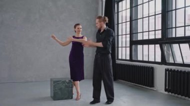 Gri stüdyoda büyük camlara karşı kadın tango öğreten bir adam.