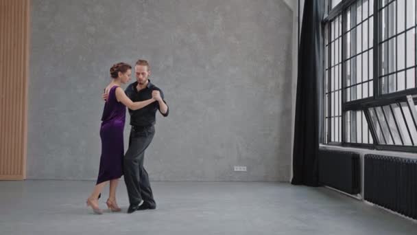 Homem e mulher estão dançando sensualmente um tango em um salão brilhante com grandes janelas — Vídeo de Stock