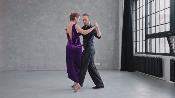 Mężczyzna i kobieta zmysłowo tańczą tango w szarym studio z dużymi oknami — Wideo stockowe