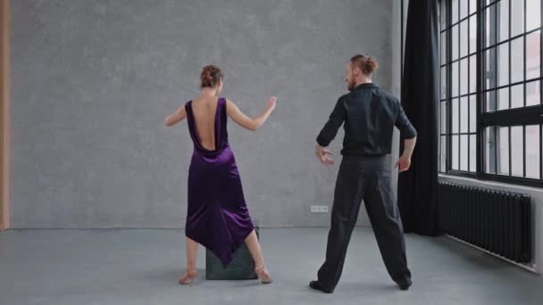 Homem ensinando mulher dançando tango no estúdio cinza contra grandes janelas — Vídeo de Stock