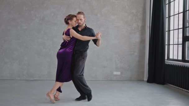 Câmera movendo-se lentamente para um par dançando sensualmente um tango em um estúdio cinza — Vídeo de Stock