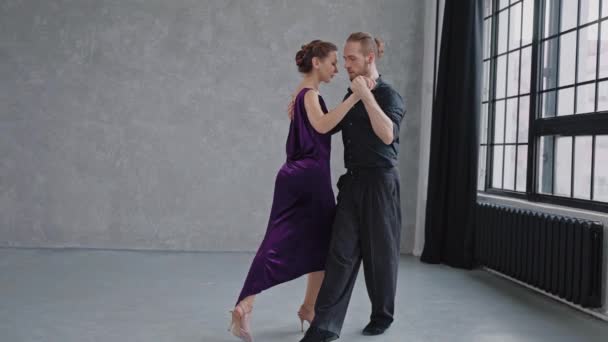 Tiro de crescimento total de um par dançando tango em estúdio cinza com grandes janelas — Vídeo de Stock