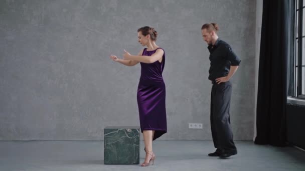 Hombre enseñando a mujer bailando tango en estudio gris contra grandes ventanales — Vídeo de stock