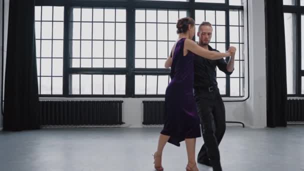 Tiro de um par sensualmente dançando um tango contra o fundo de grandes janelas — Vídeo de Stock