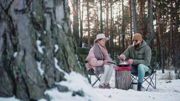 Pareja cocinando el almuerzo en el campamento en el bosque en un día soleado de invierno — Vídeo de stock