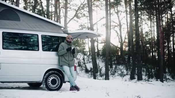 Чоловік п'є, стоячи в задній частині фургона з вискоченим дахом в лісі взимку — стокове відео
