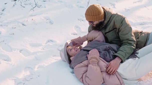 Romantikus boldog pár fekszik a hóban, és nevetni a napsütéses napon, élvezi az életet — Stock videók