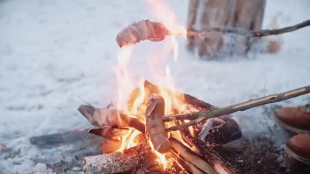 Близкий снимок жареных сосисок на палочках на костре зимой — стоковое видео