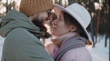 Romantik, şık bir çift, güneşli bir kış gününde ormanda konuşur ve öpüşür.