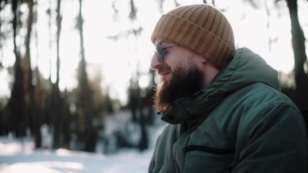 Handsome man drinking hot drink in the woods in winter, enjoying camp life — Stock Video