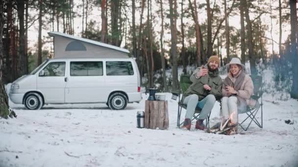 Пара мандрівників сидить біля багаття і бере селфі в лісі взимку — стокове відео