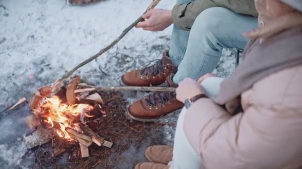 Люди обсмажують ковбаски на паличках на багатті в лісі взимку — стокове відео