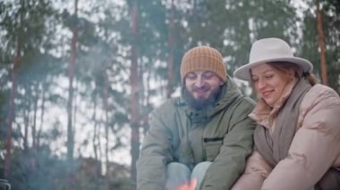 Çiftler kışın ormanda kamp ateşinde ellerini ısıtıyorlar.