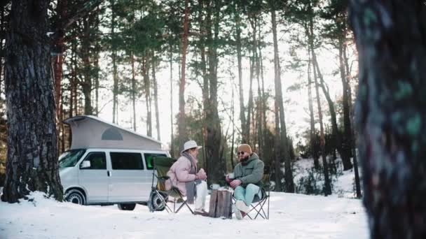 Пара мандрівників відпочиває в лісі в сонячний зимовий день, насолоджуючись життям фургона — стокове відео