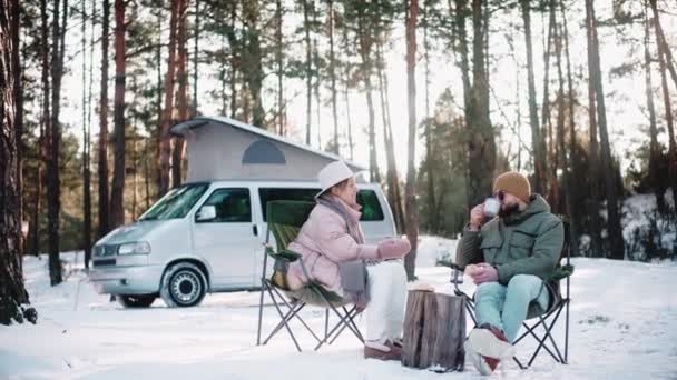 Пара мандрівників відпочиває в лісі в сонячний зимовий день, насолоджуючись життям фургона — стокове відео