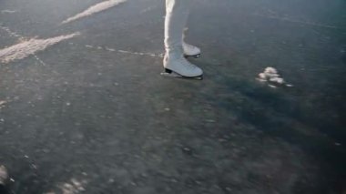 Güneşli bir kış gününde, açık bir gölde beyaz pantolonla buz pateni yapan kadın.