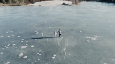 Güzel güneşli bir arazide donmuş bir gölde kayan çiftin hava görüntüsü.