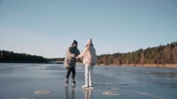 Hombre enseñando a la mujer a patinar sobre hielo en un lago congelado en un día soleado de invierno — Vídeos de Stock
