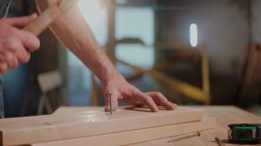 Stüdyoda tahta tahtada çekiçle çivi çakan bir adamın yakın plan fotoğrafı.