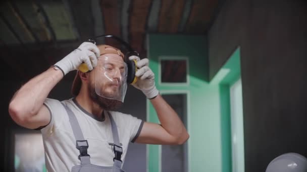 Construtor masculino tira óculos de segurança e fones de ouvido após o trabalho em estúdio — Vídeo de Stock