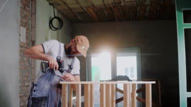 Erkek inşaat işçisi stüdyoda tahta bir yapıya vida vidalıyor.