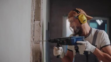 Duvara çekiç matkabıyla delik açan, güvenlik gözlüğü ve kulaklık takan biri.