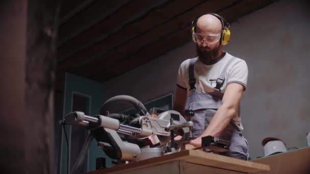 Um construtor corta uma tábua de madeira em uma serra circular de mesa no estúdio de construção — Vídeo de Stock