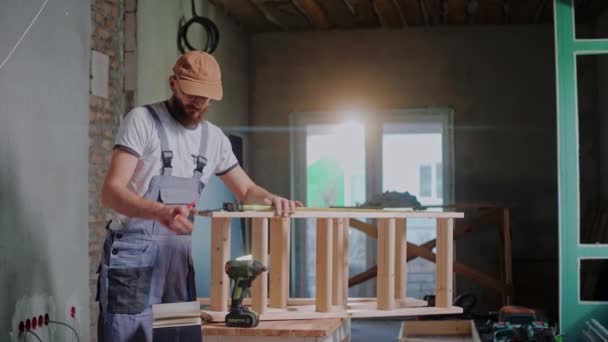 Construtor masculino usa uma fita métrica para medir a construção de madeira e escreve notas — Vídeo de Stock