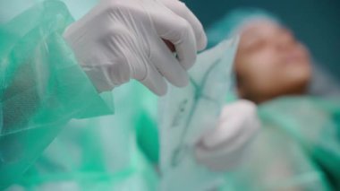 Hemşirenin steril torbadan cerrahi makası çıkardığı yakın çekim.