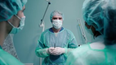 Cerrah koruyucu maske ve cübbe giyen insanlarla konuşuyor.
