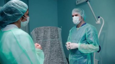 Cerrah ameliyattan önce koruyucu eldiven ve önlük giymiş bir hastayla konuşur.