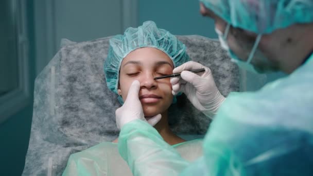 Chirurg vyšetřuje dívky tvář před operací nosu, kreslení na nose — Stock video
