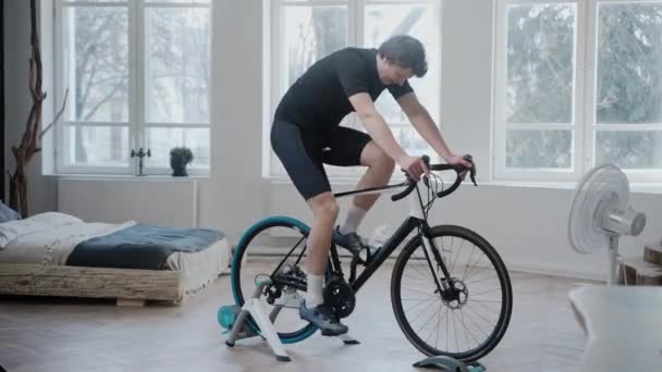 Vista lateral de um ciclista treinando em uma bicicleta de exercício que fica em casa — Vídeo de Stock
