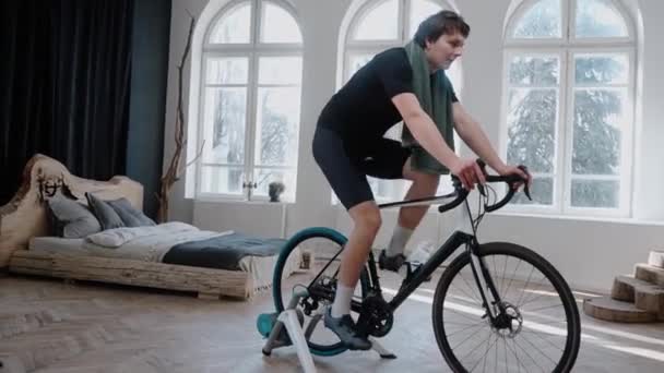Um ciclista treinando em uma bicicleta de exercício em casa e respirando pesadamente — Vídeo de Stock