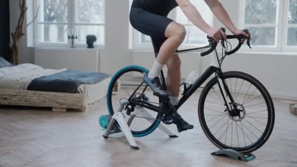 Tiro de parte inferior do corpo de um ciclista que treina em uma bicicleta de exercício em casa — Vídeo de Stock