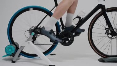 Parlak beyaz bir stüdyoda egzersiz bisikleti süren bir bisikletçinin yakın çekimi.