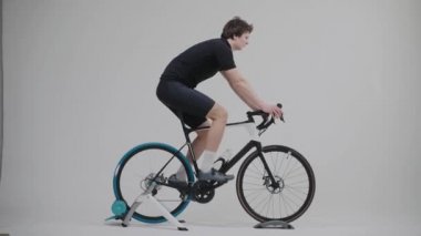 Parlak beyaz bir stüdyoda egzersiz bisikletine binen bir bisikletçinin yan görüntüsü