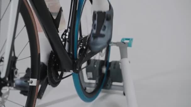 Tiro das pernas de um ciclista treinando em uma bicicleta de exercício em estúdio branco — Vídeo de Stock