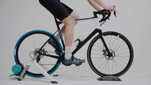 Foto de las piernas de un ciclista entrenando en una bicicleta estática en un estudio blanco — Vídeo de stock