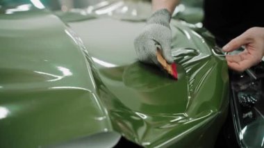 Plastik kartlarla arabanın kaputunu koyu yeşil renge sarma işlemi. Bir araba stüdyosunda araba kaputu sarma işlemi. Parlak haki rengi yeşil araba plastiği. Yüksek kalite 4k görüntü